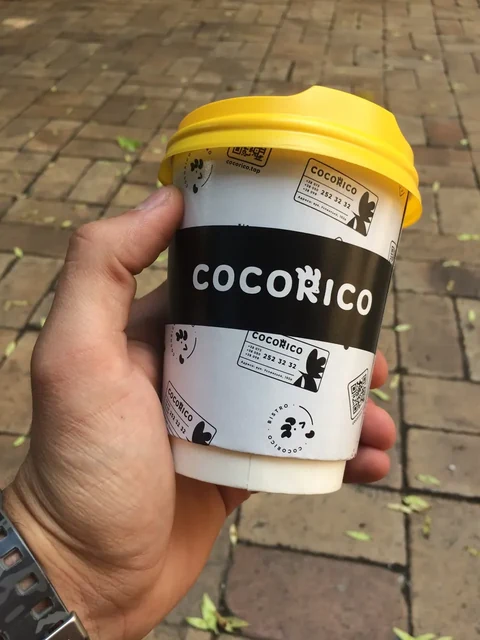 Рука держит стакан Cocorico с жёлтой крышкой на улице — ИЗДИДЖИТЛ